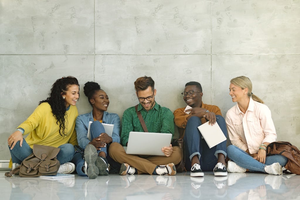 Students using their laptop while sitting down in the campus hallway